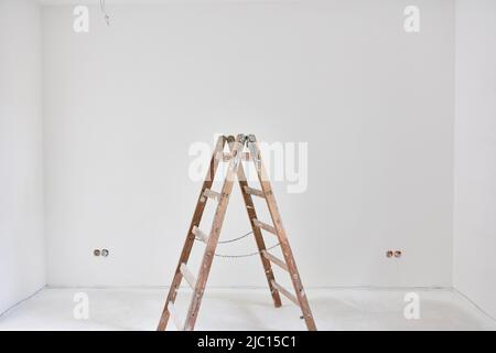 Wooden ladder in front of a white wall after painting in the house Stock Photo