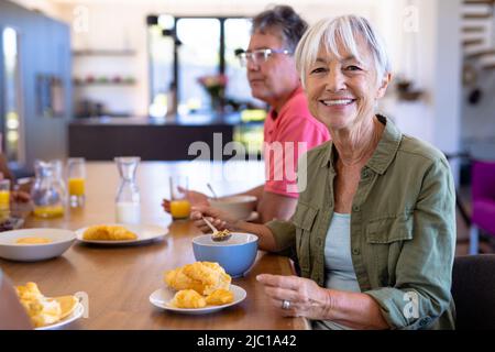 Portrait of smiling asian senior woman having breakfast with caucasian man at dining table Stock Photo