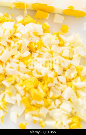Cutting hard-boiled eggs in a shape of a loaf on a white cutting board. Stock Photo