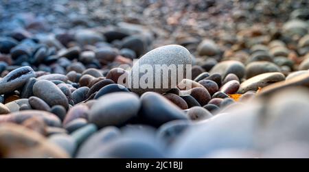 Rounded boulders of different sizes and colors on a beach in an atmosphere of tranquility and peace with a white stone in focus in the foreground Stock Photo