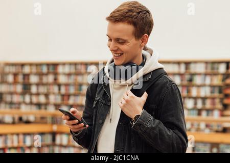 Smiling student using smartphone while standing in library Stock Photo