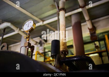 Pressure valve dial in a steam power boiler room. Steam tanks with pipes and lagging. Stock Photo