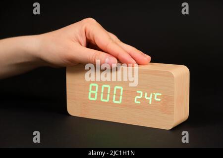 A digital clock showing a time of eight o'clock in the morning and a woman's hand on a black background Stock Photo