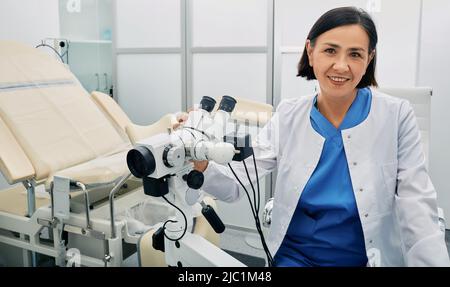 Portrait of gynecologist sitting near gynecological chair and ...