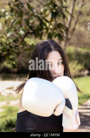 young female boxer with white gloves in a park Stock Photo