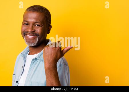 Portrait of positive glad person indicate thumb finger empty space isolated on yellow color background Stock Photo