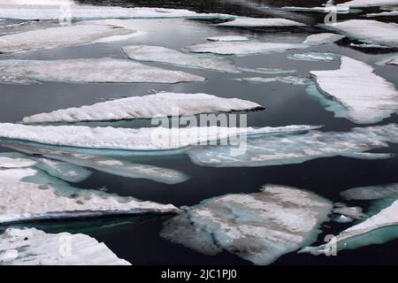 Ice floe melting on mountain lake. Cracked ice blocks covered with snow floating in the water. Ice on the water abstract background. Stock Photo