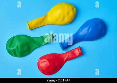 Multi-colored not inflated balloons red, yellow, blue, green lie diagonally on a blue background. Top view Flat lay Stock Photo