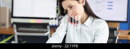 Woman worker talking on phone and making notes on paper in personal office Stock Photo