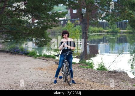 Woman 40-44 years old on a bicycle. The girl decided to get in shape for the beginning of summer. Stock Photo