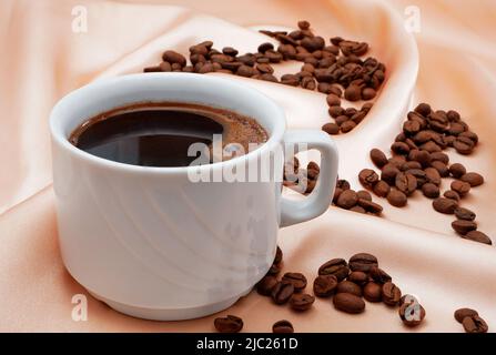 cup of black coffee on pink satin with roasted coffee beans Stock Photo