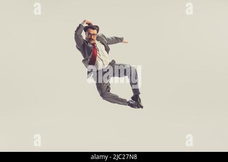 Emotional jumping man, businessman wearing grey striped suit in 50s, 60s fashion style flying isolated on white background. Retro vintage style Stock Photo