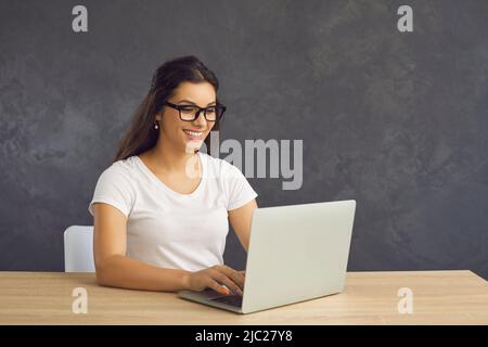Positive woman working, shopping online or corresponding with friends while sitting at a laptop. Stock Photo