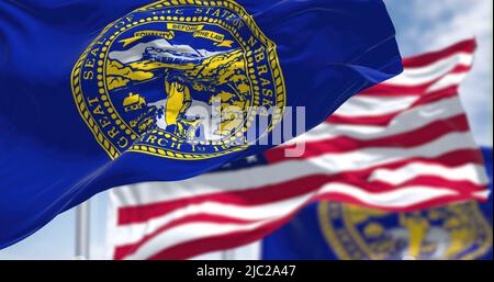 The Nebraska state flag waving along with the national flag of the United States of America. In the background there is a clear sky. Nebraska is a sta Stock Photo