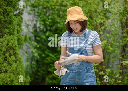 An Asian woman gardener is taking off her gloves after finishing her work. Stock Photo