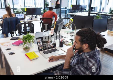 Biracial businessman sitting at desk in office during online meeting with multiracial colleagues Stock Photo