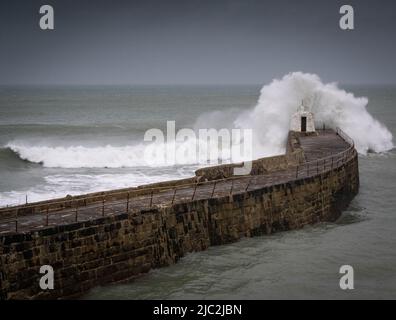 Wave crashing over the Monkey Hut at the end of Portreath harbour wall, Cornwall Stock Photo