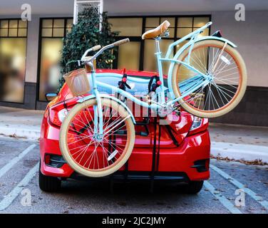 Blue bicycle with basket fastened to back of red sports car parked in front of shops Stock Photo