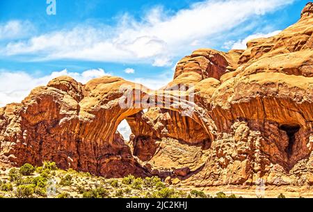 Famous Double Arches aka The Spectacles in Arches National Park in Utah USA with tiny ant-sized tourists exploring inside Stock Photo