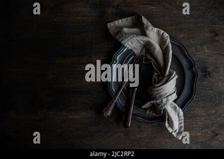 Overhead view of a black cutlery set on a black plate and black table Stock Photo