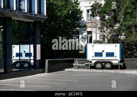 Backup Generator on the trailer with wheels. Mobile emergency Generator or Standby Generator - Outdoors Power Equipment on parking nearby glass office Stock Photo