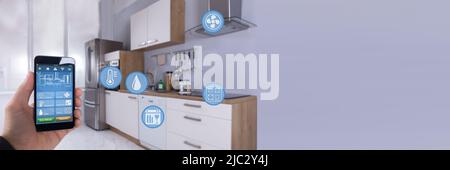 Close-up Of A Person's Hand Using Smart Home Application On Smartphone In Kitchen Stock Photo