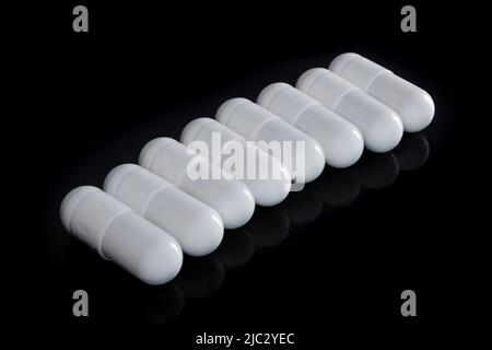 White capsules in a row isolated on black background with reflection . Medications, nutritional supplements. Pharmaceutical industry concept. Stock Photo