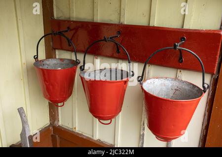 Three traditional fire buckets hanging on a wall at Bolton Abbey railway station, Yorkshire, UK Stock Photo