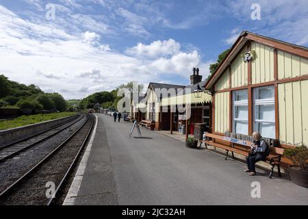 Woman sitting on bench and people walking on platform between colourful yellow wooden train station building and rails at Bolton Abbey railway station Stock Photo