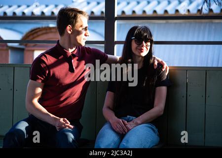 Young pretty woman smiles as her man hugs her while they sit on a sunny early June day on the roof in Kiev Podol (Low town) district Stock Photo