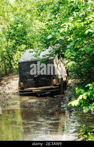 Back view of green russian off-road utility vehicle UAZ Hunter broke down, jammed on dirty road in forest among trees. Stock Photo