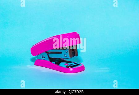 small pink stapler for paper, on a blue background. item used for office work and document archiving. practical portable stapler. Stock Photo