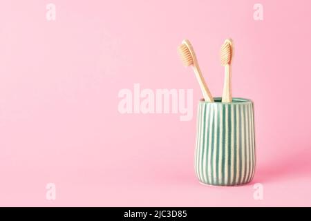 Two bamboo toothbrushes in a green ceramic holder on a pink background. Eco-friendly, zero-waste concept. Copy space for text, selective focus Stock Photo