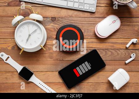 Different gadgets uncharged mobile phone and alarm clock on wooden background Stock Photo