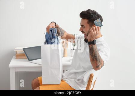 Happy young man with credit card taking new clothes from shopping bag at home Stock Photo