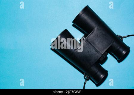 close-up detail of binoculars, on a blue background. concept of travel, search and sighting of birds. small black binoculars for children. space for c Stock Photo
