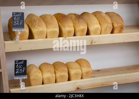 Bricks of wheat bread lie on wooden shelves in store. Fresh delicious of bread loaves in bakery, baker shop. High quality photo Stock Photo