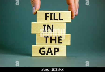 Fill in the gap symbol. Concept words Fill in the gap on wooden blocks on a beautiful grey table grey background. Businessman hand. Business, motivati Stock Photo