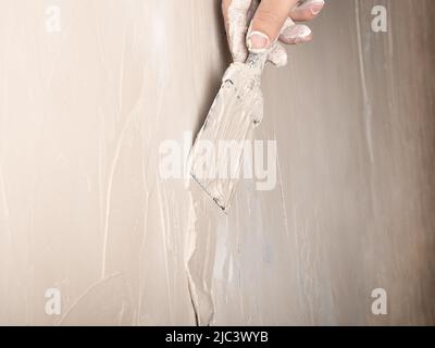 hand application of wall putty with a spatula closeup, plaster repair work. Stock Photo