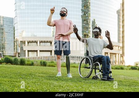 Multiracial friends with disability using augmented reality futuristic glasses outdoor at park city - Focus on African man sitting on wheelchair Stock Photo