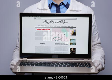 Closeup on modern medical doctor woman in white medical robe showing laptop with monkeypox news against grey background. Stock Photo