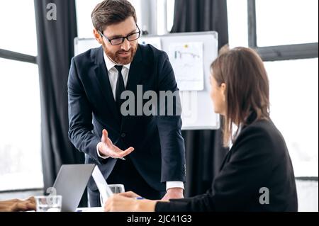 Conversation of two coworkers. Successful smart business colleagues, caucasian man and woman, in a modern office, discussing a new project, a financial business plan, future strategy Stock Photo