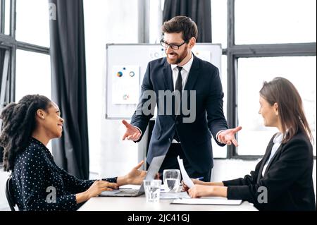 Teamwork of multiracial employees, collaboration. Caucasian attractive male boss, discussing ideas for a new business project, brainstorming, explaining financial business plan to his female partners Stock Photo