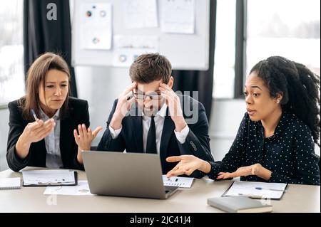 Irritated business employees of a different nationalities are sitting at the workplace in a modern office, argue over work issues, cannot agree, experience stress from working together Stock Photo