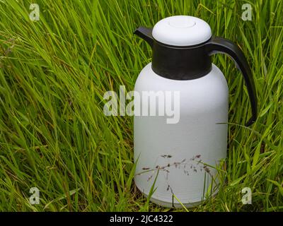 White thermo bottle isolated on green grass. A hot drink thermos on a grass in the park. Nobody, selective focus, copy space for text Stock Photo