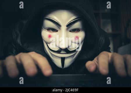Hacker cracker With anonymous association mask working on the laptop. Anonymous is a loosely associates international network of activist and hacktivi Stock Photo