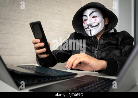 Hacker in the mask of anonymus using mobile phone Stock Photo