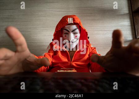 Hacker cracker With anonymous association mask working on the laptop. Anonymous is a loosely associates international network of activist and hacktivi Stock Photo