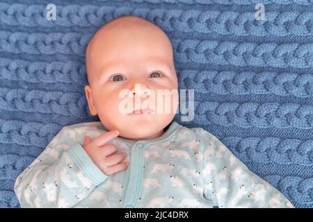 Portrait of a cute 3-month-old baby, a newborn boy lying in a bad. Newborn child relaxing in bedroom. Family morning time at home. Stock Photo