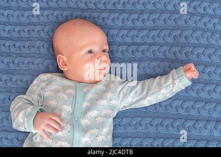 Portrait of a cute 3-month-old baby, a newborn boy lying in a bad. Newborn child relaxing in bedroom. Family morning time at home. Stock Photo